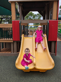 two girls in pink dresses race down yellow slides at the Destination Playground in Willmar, MN